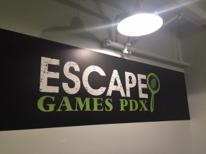 An Escape Games PDX sign hangs on the wall in the lobby under a lamp.